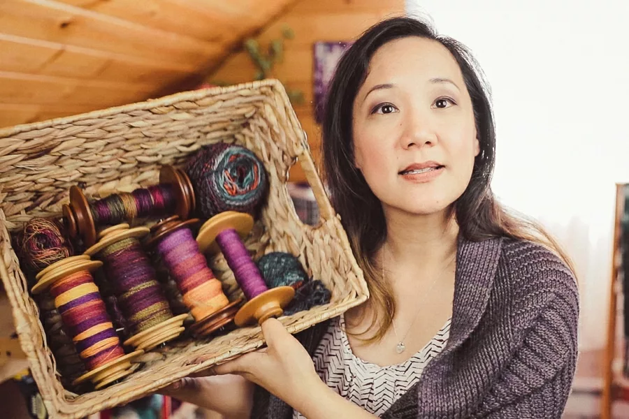 Felicia Lo Wong holding up a basket of five bobbins of handspun yarns