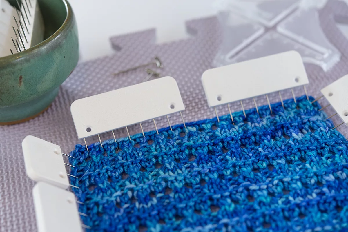 blocking a blue knitted lace swatch with blocking pins