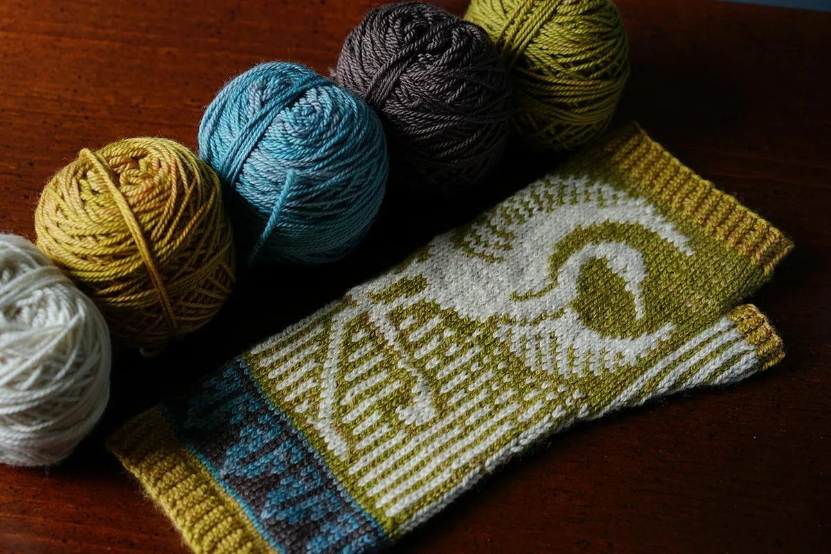 Thula mitt pattern featuring a white egret on yellow, blue, and brown party of five yarns