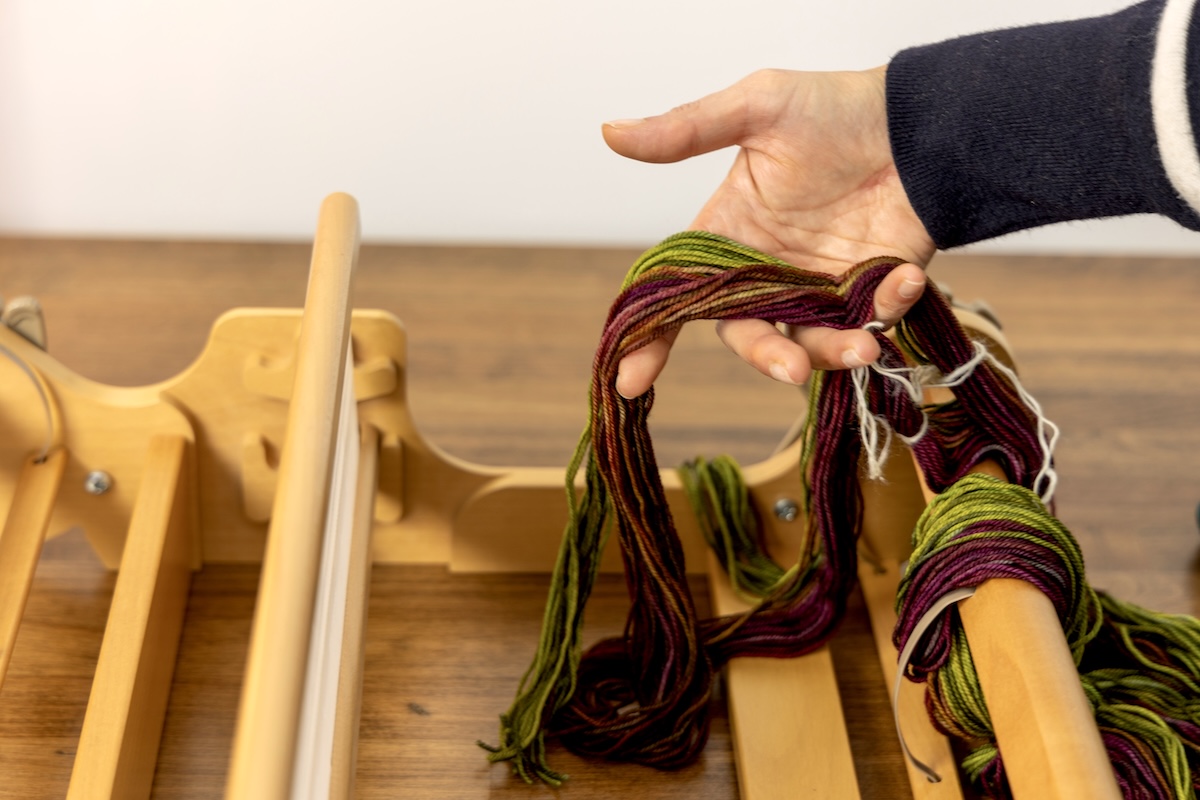Someone is using their hand to keep the warp cross secure with the warp ends cut open on the other side.