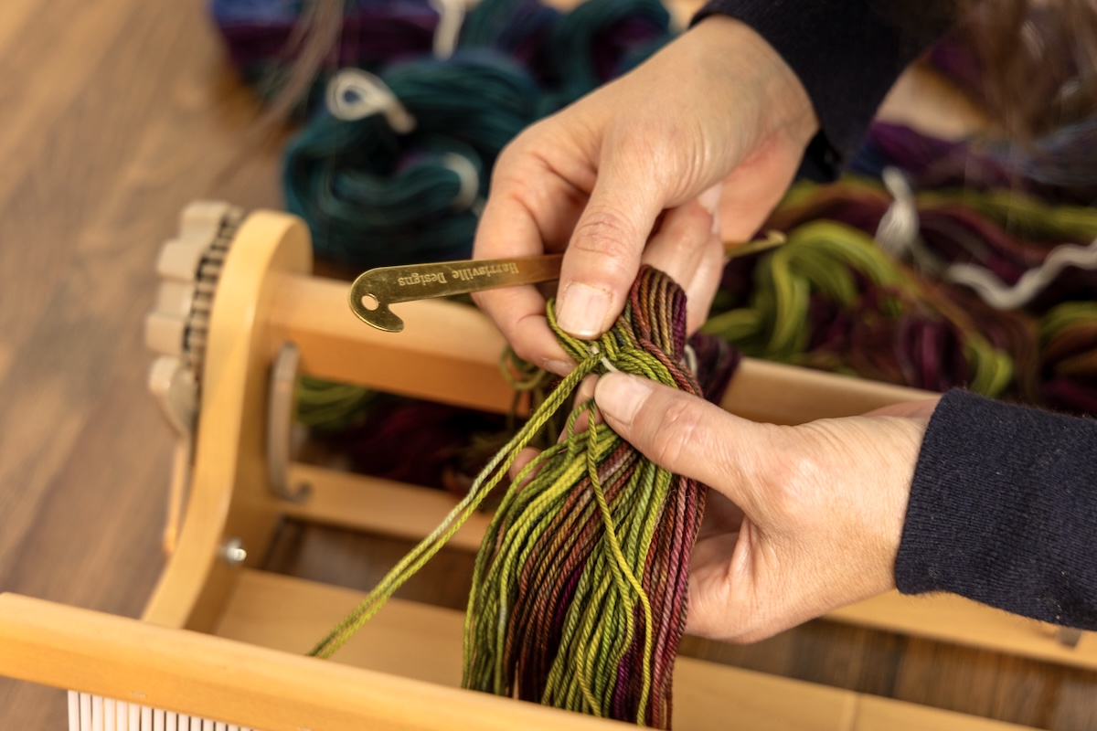 Someone is slowly separating the warp threads while keeping the cross secure in their hands at the same time.