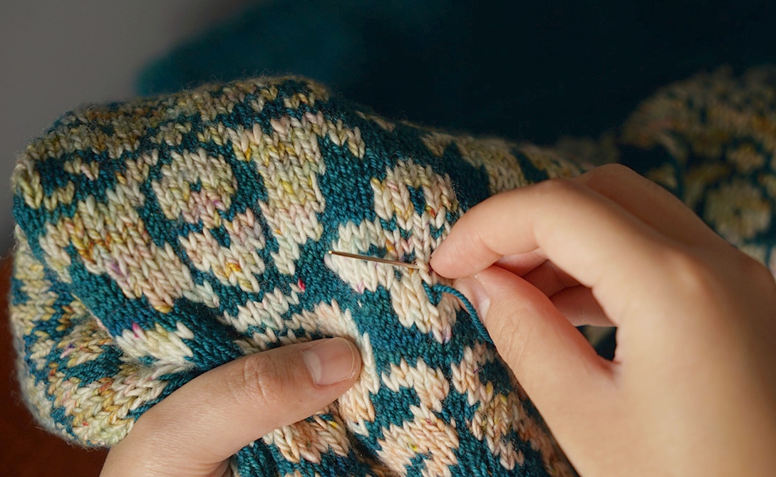 Ruth using duplicate stitch on a knitted sweater