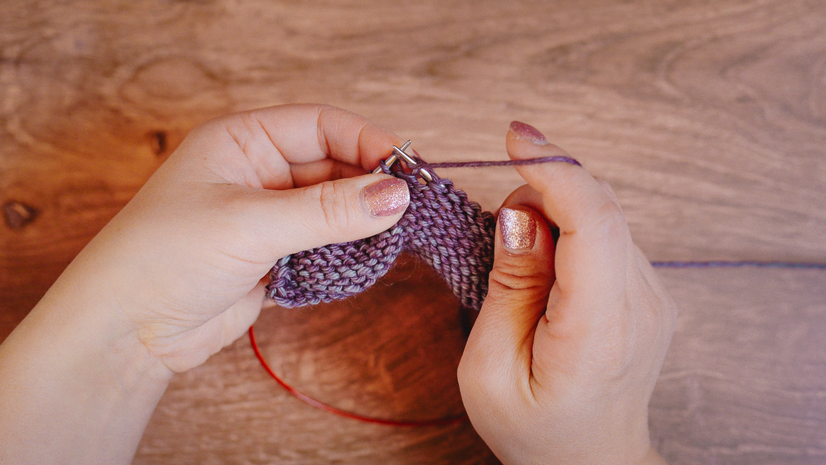 New purl stitch forming on the tip of the right needle.