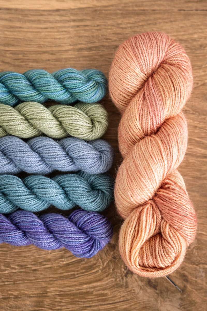 Summer Spectra Knit-Along 2026 Trifecta Fine in Black Raspberry, Glow, or London Fog (MC) plus Lavender, Mermaid, Blue Canoe, Clearwater, and Sage Trifecta Fine mini-skeins (CC)