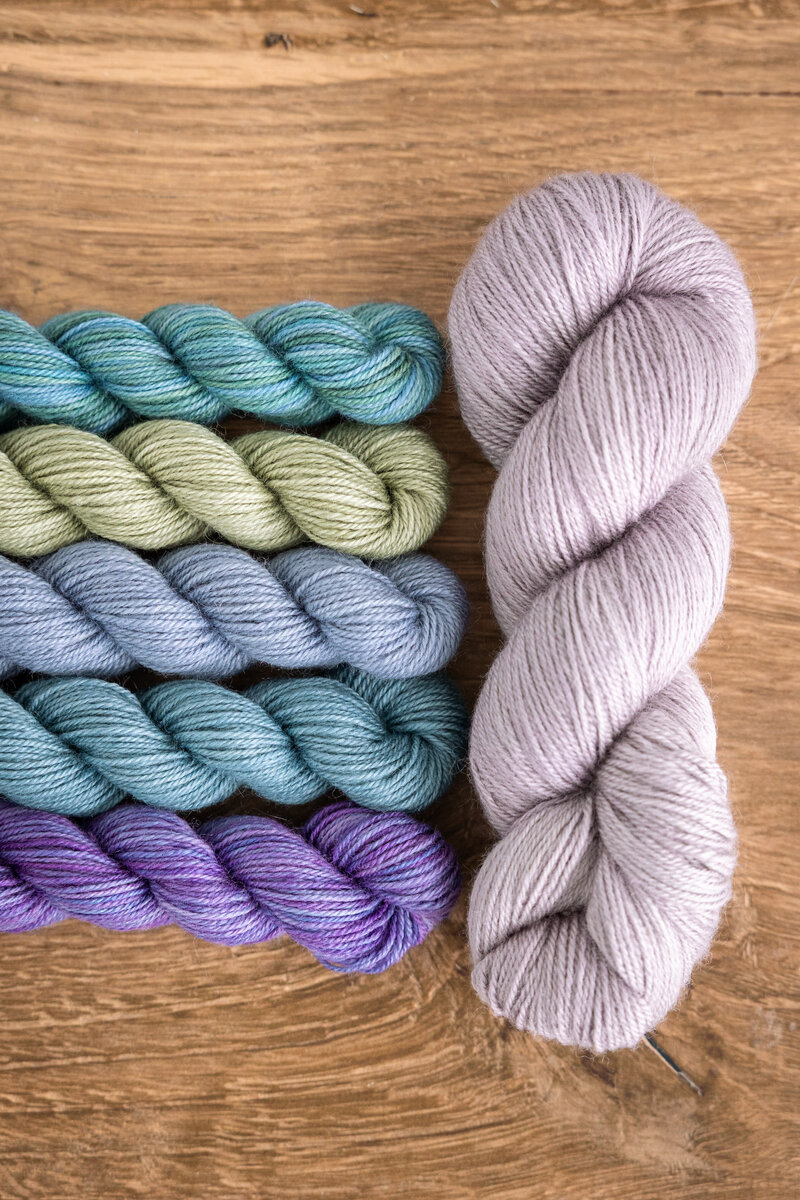 Summer Spectra Knit-Along 2026 Trifecta Fine in Black Raspberry, Glow, or London Fog (MC) plus Lavender, Mermaid, Blue Canoe, Clearwater, and Sage Trifecta Fine mini-skeins (CC)