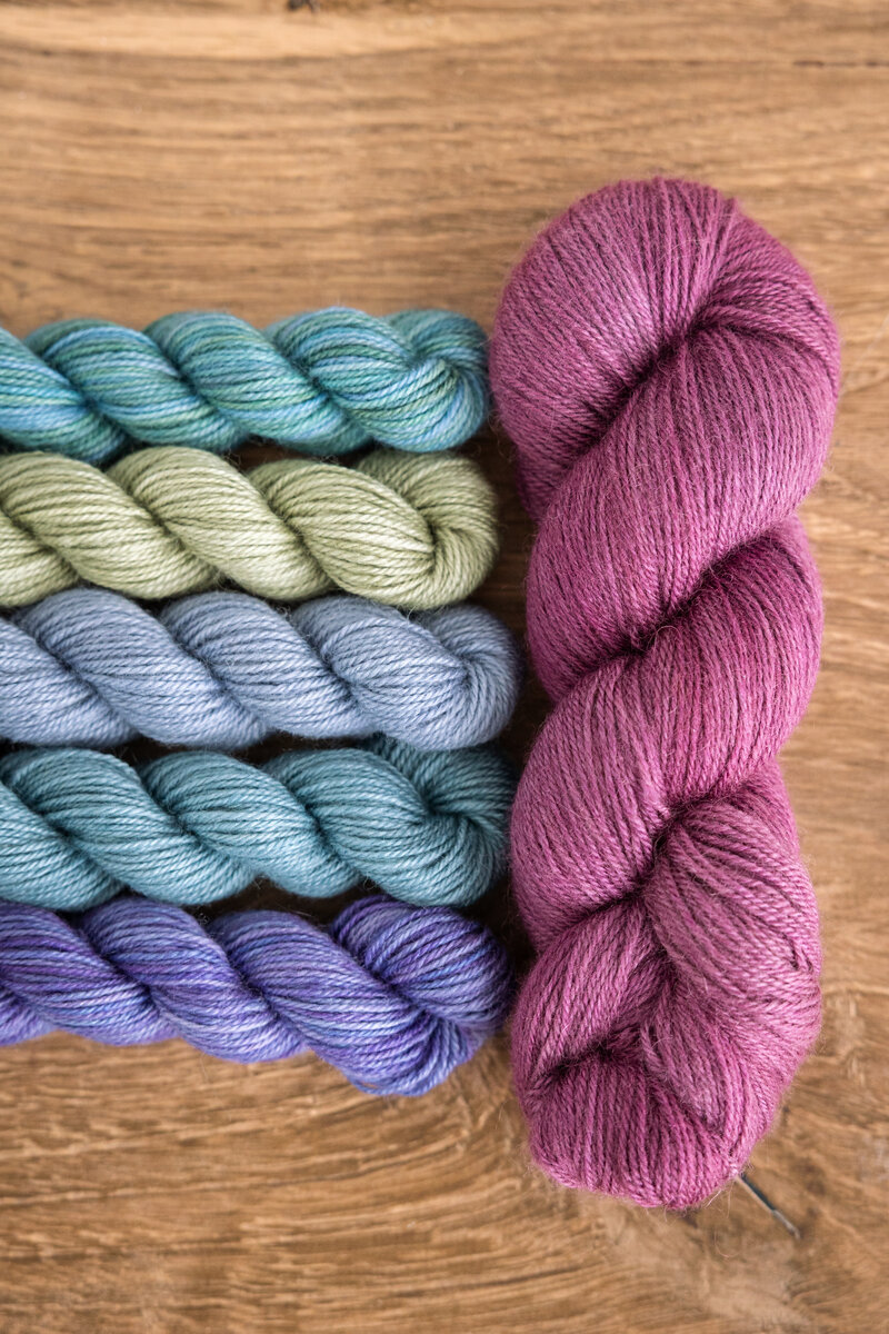 Summer Spectra Knit-Along 2026 Trifecta Fine in Black Raspberry, Glow, or London Fog (MC) plus Lavender, Mermaid, Blue Canoe, Clearwater, and Sage Trifecta Fine mini-skeins (CC)