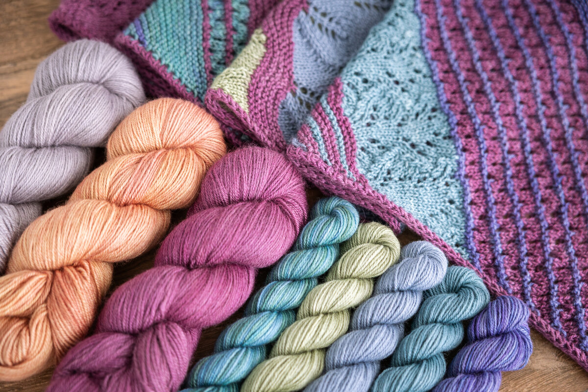 Summer Spectra Knit-Along 2026 Trifecta Fine in Black Raspberry, Glow, or London Fog (MC) plus Lavender, Mermaid, Blue Canoe, Clearwater, and Sage Trifecta Fine mini-skeins (CC)